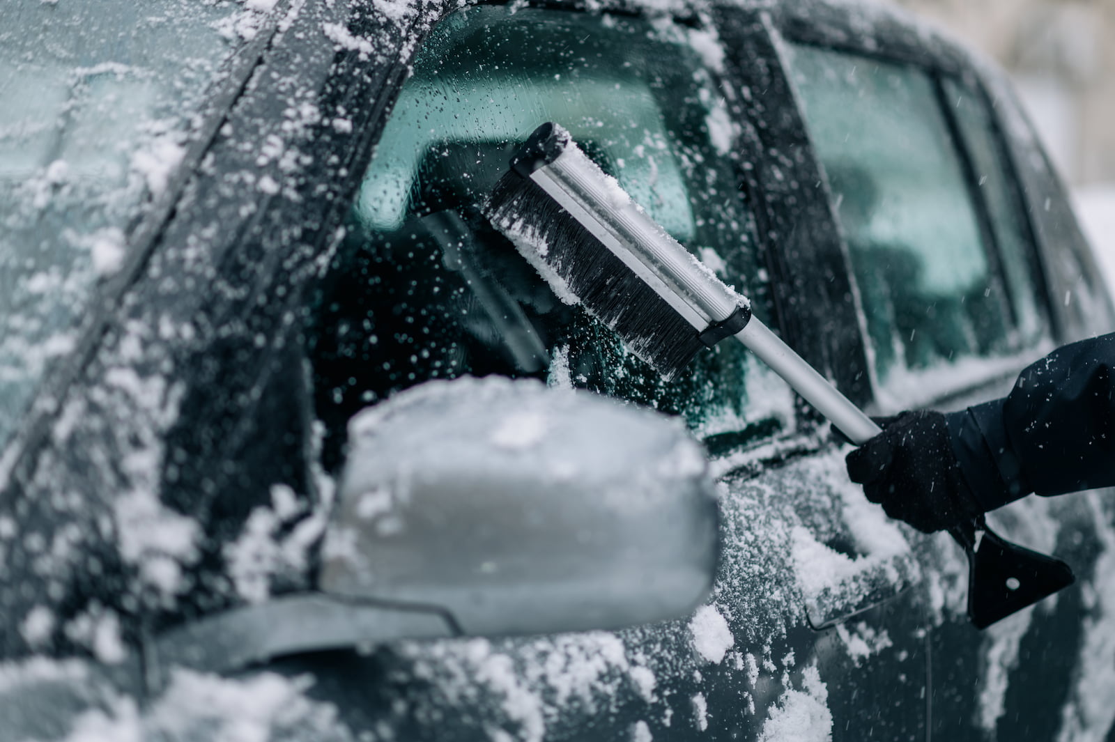 Person clearing snow off car in winter