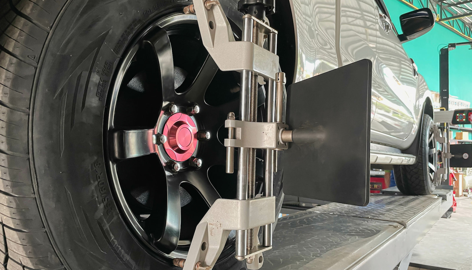 Wheel alignment sensor attached to black alloy wheel on raised SUV in service bay.