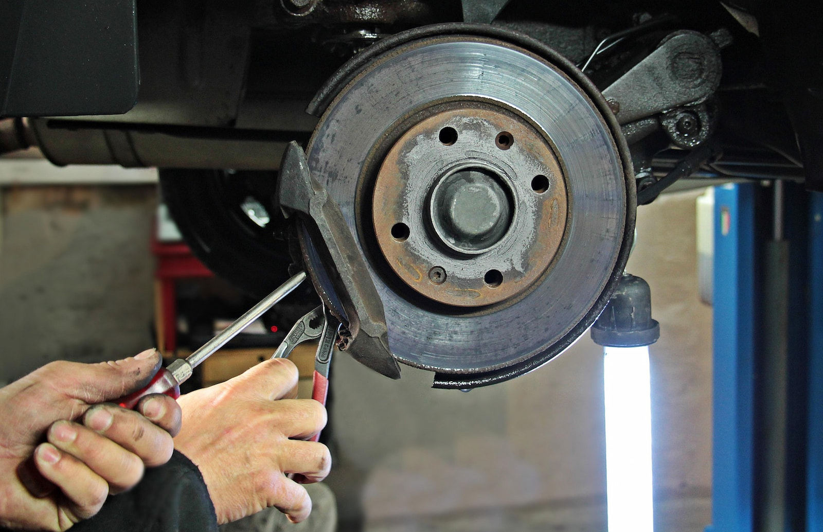 Mechanic removing worn brake pad from disc brake assembly in Menasha, WI auto repair shop.