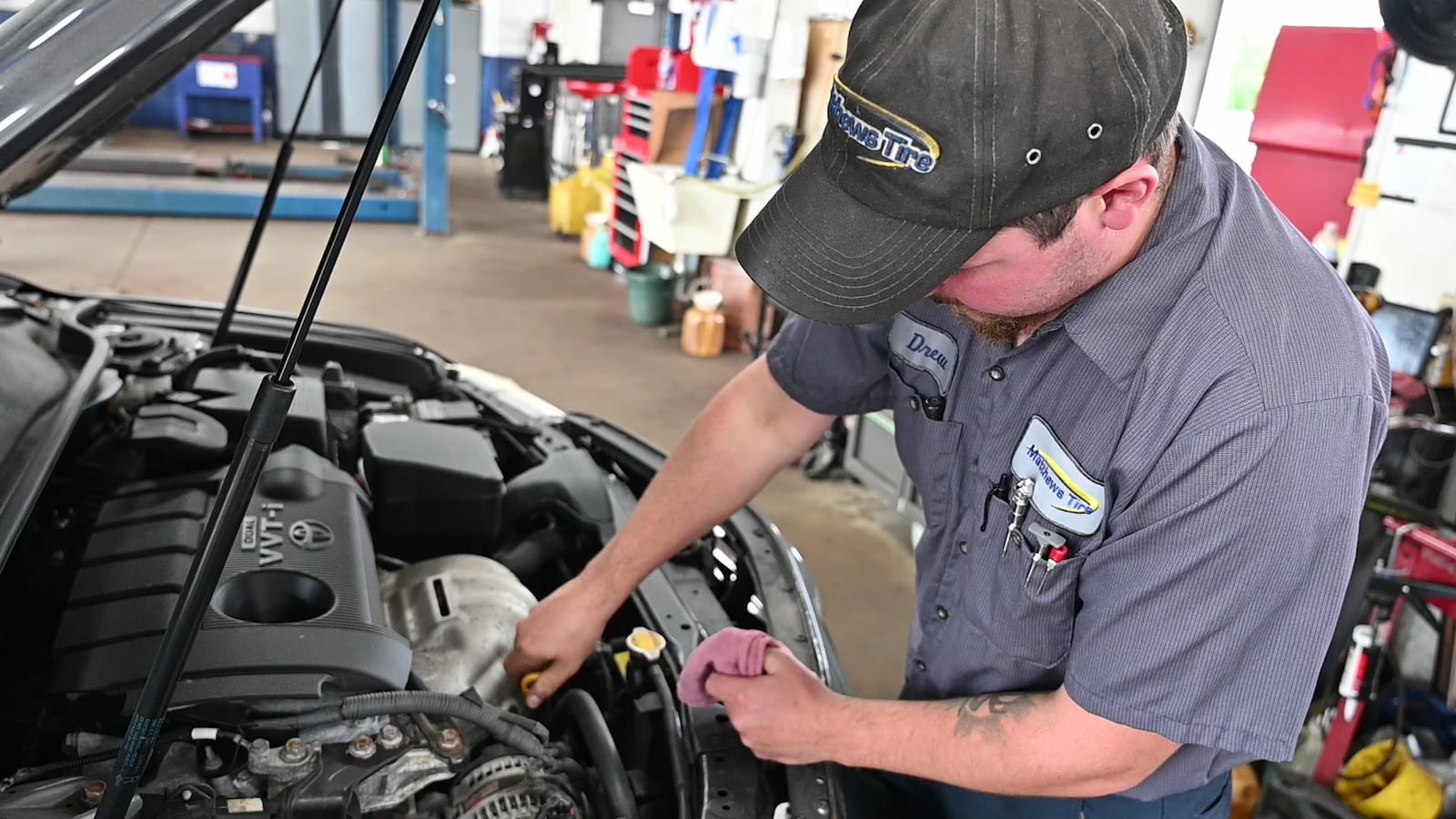 Matthews Tire technician inspecting vehicle engine during AC repair in Fond du Lac, WI.