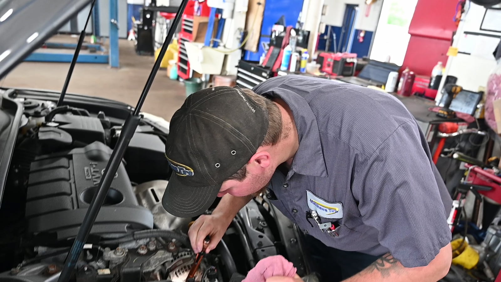 Matthews Tire technician inspecting engine components during car AC service in Green Bay, WI.