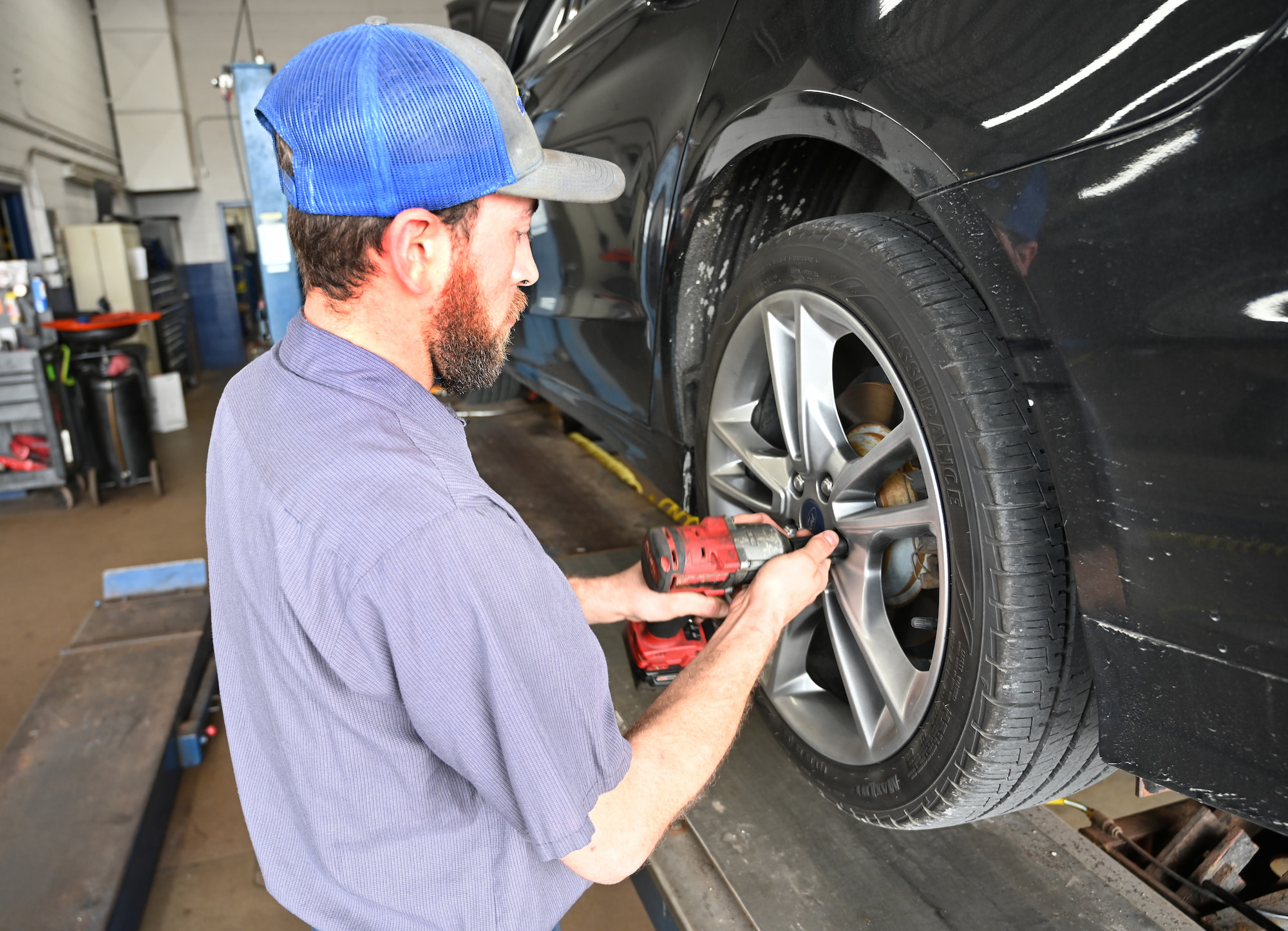 Auto mechanic using impact wrench for tire rotation on black sedan in Appleton, WI.