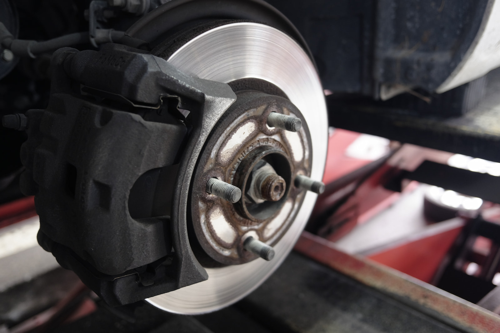 Close-up of new brake rotor and caliper on vehicle lift at brake shop in Appleton, WI.