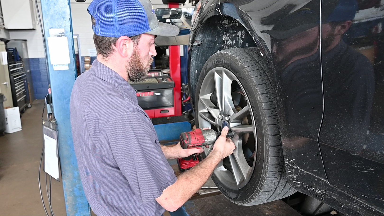 Auto mechanic using impact wrench for tire rotation on black Ford sedan in Green Bay, WI.