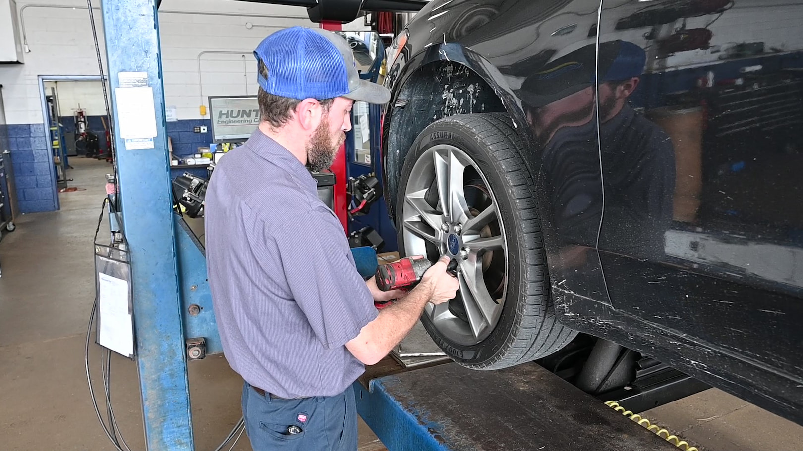 Auto technician using power tool to rotate front tire on Ford sedan in Menasha WI.
