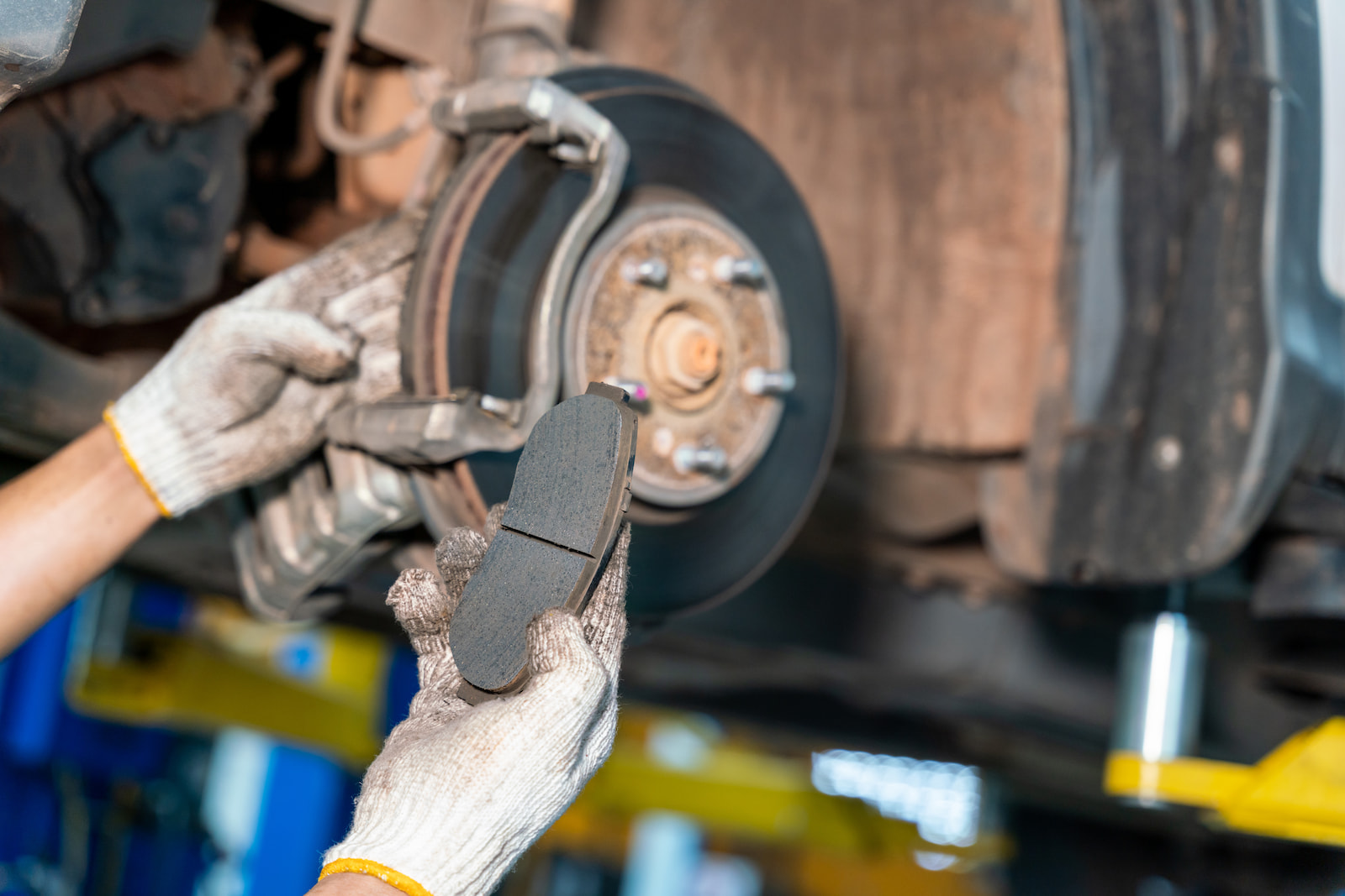 Mechanic installing new brake pad on front disc brake at auto repair shop in Waupaca, WI.