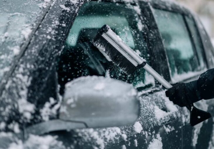 person-clearing-snow-off-car-in-winter